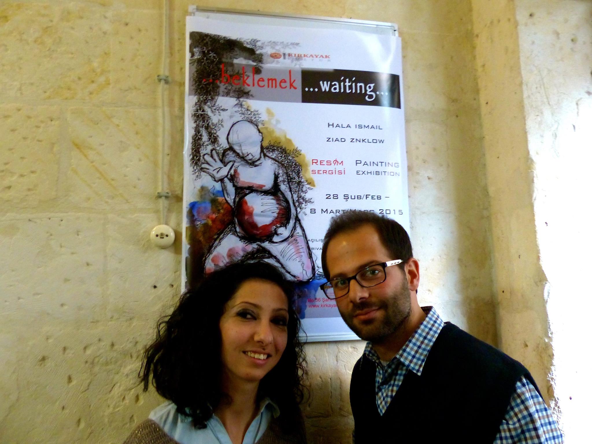 Hala and Ziad, two Syrian refugee artists who benefitted from their residency at Kırkayak. They stand in front of a poster for their 2015 exhibition, "Beklemek / Waiting". 